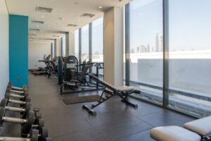 Contemporary gym with exercise equipment and Dubai skyline view through large windows.
