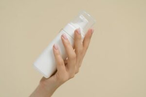 A close-up of a hand holding a white cosmetic bottle against a neutral background, perfect for product mockups and beauty industry use.