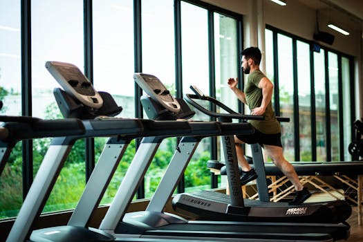 Best Home Treadmills of 2025 for Every Fitness Level Young man workouts on treadmill in modern gym with large windows and natural light.
